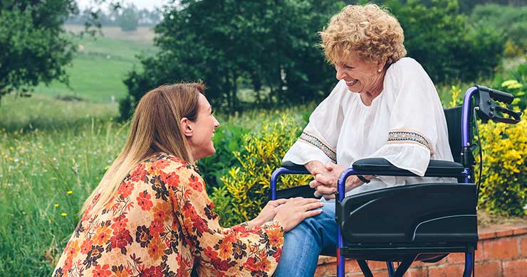 Carer kneeling beside woman in wheelchair